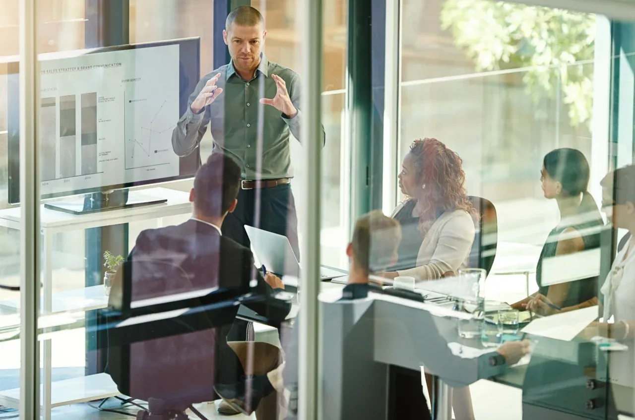 A team gathered in a glass-walled conference room during a presentation