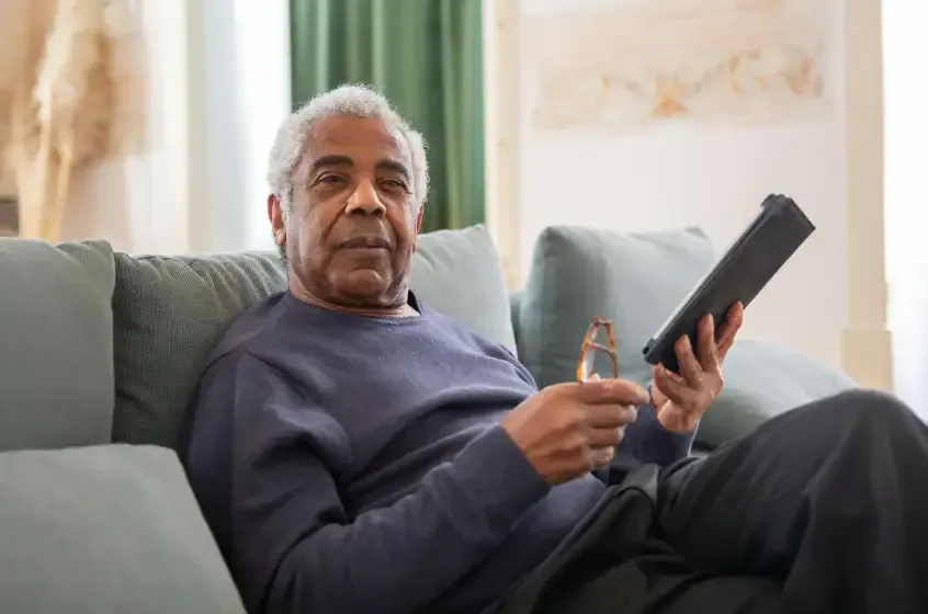 Retired man relaxing on a couch and reading on a tablet